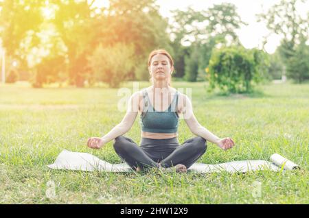 Eine Frau mittleren Alters praktiziert Yoga im Freien. Frau, die im Park in Lotusposition meditiert Stockfoto