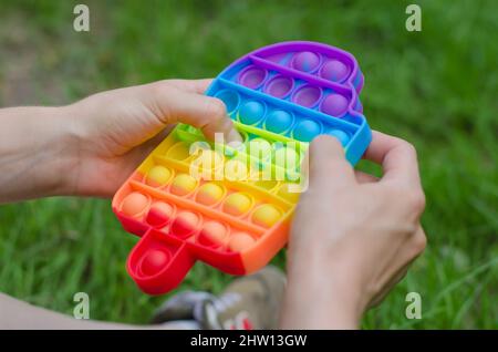 In Form von Eis in weibliche Hände zappelig einschlagen. Mädchen in der Natur spielt mit Pop it Stockfoto
