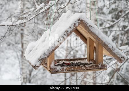 Schneebedeckte Vogelfutterstelle aus Holz, die im Winterwald hängt Stockfoto