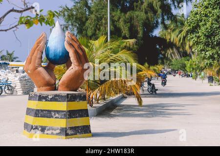 Maafushi, Malediven - 25. Juni 2021: Lokales Denkmal mit gefalteten Händen und Blue Water Drop an der Maafushi Straße Stockfoto