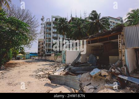 Ruinen der Holzhäuser mit dem maledivischen Hotelgebäude im Hintergrund, Maafushi Island Stockfoto