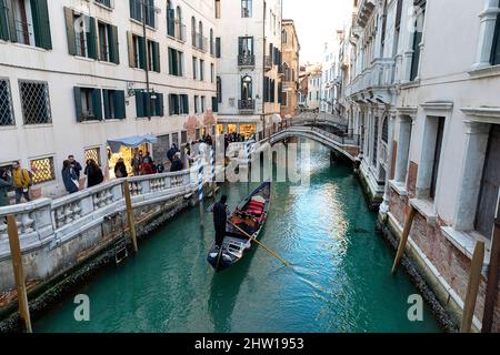 Traditionelles venezianisches Gondelboot mit Touristen, die an einem Karnevalstag, Italien, den engen Kanal erkunden, umgeben von traditionellen mittelalterlichen Häusern in Venedig Stockfoto