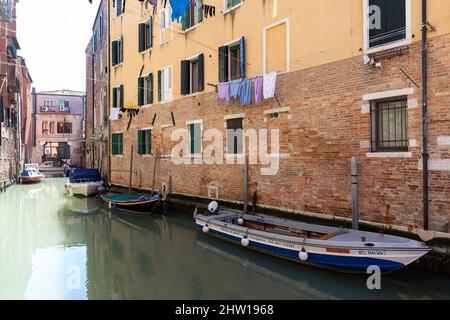 Altes Haus in der Nähe eines Wasserkanals in Venedig, geparkte Holzprahlerei und Wäschetrocknung unter den Fenstern eines sonnigen Frühlingstages, Venedig, Italien Stockfoto