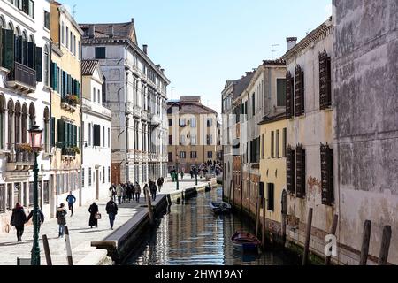 Einheimische und Touristen auf einer Straße in der Nähe eines Wasserkanals in Venedig an einem Karnevalstag an einem schönen sonnigen Tag, Venedig, Italien Stockfoto