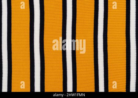 Kuscheliger Hintergrund aus gelbem Strickpullover mit weißen und schwarzen Streifen. Stockfoto