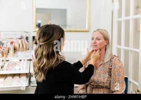 Kosmetikerin, die Foundation Make-up auf eine blonde Frau in einem Schminkstuhl anwendet Stockfoto