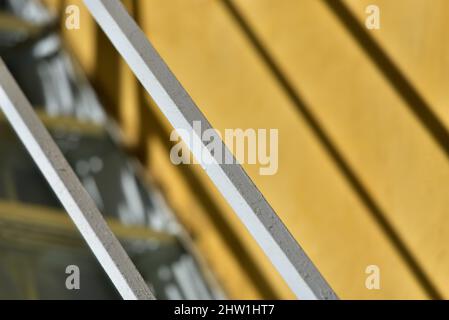 Abstrat mit einer handgefertigten schmiedeeisernen Treppengeländer an einer ockerfarbenen Stuckwand in Nafplio, Griechenland. Stockfoto