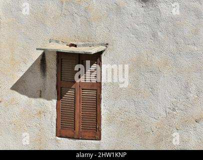 Altes traditionelles ländliches Haus, braunes Holzfenster mit Fensterläden und einem Baldachin auf einer verwitterten venezianischen Stuckwand in Nafplio, Griechenland. Stockfoto