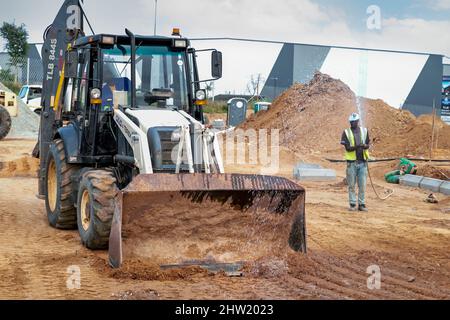 Kapstadt, Südafrika, 24.. Februar - 2022: Mann sprüht Wasser vor dem Bagger, um Staub auf der Baustelle zu halten. Stockfoto