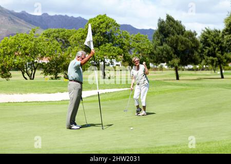 So nah dran. Eine ältere Dame, die ihre Faust in Enttäuschung hochhält, während sie während eines Golfspiels einfach das Loch verpasst. Stockfoto