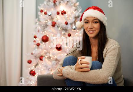 Einfach unvergleichlich... Kakao am Weihnachtsmorgen. Porträt einer attraktiven jungen Frau, die beim Weihnachtskaffee eine Tasse Kaffee trinkt. Stockfoto