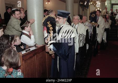 Die neue Sefer Tora wird um die Synagoge getragen, damit die Gemeinde ihre Achtung zollt. Der Oberrabbiner Jonathan Sacks war Ehrengast für die Aufnahme der letzten Briefe in eine neue Sefer-Torah in der Synagoge der hebräischen Kongregation Singers Hill am Sonntag, dem 15. März 1998. Mitglieder der Gemeinde sowie der Oberrabbiner fügten jeweils einen einzigen Brief hinzu. Stockfoto