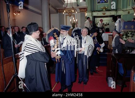 Die neue Sefer Tora wird um die Synagoge getragen, damit die Gemeinde ihre Achtung zollt. Der Oberrabbiner Jonathan Sacks war Ehrengast für die Aufnahme der letzten Briefe in eine neue Sefer-Torah in der Synagoge der hebräischen Kongregation Singers Hill am Sonntag, dem 15. März 1998. Mitglieder der Gemeinde sowie der Oberrabbiner fügten jeweils einen einzigen Brief hinzu. Stockfoto