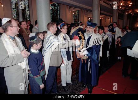 Die neue Sefer Tora wird um die Synagoge getragen, damit die Gemeinde ihre Achtung zollt. Der Oberrabbiner Jonathan Sacks war Ehrengast für die Aufnahme der letzten Briefe in eine neue Sefer-Torah in der Synagoge der hebräischen Kongregation Singers Hill am Sonntag, dem 15. März 1998. Mitglieder der Gemeinde sowie der Oberrabbiner fügten jeweils einen einzigen Brief hinzu. Stockfoto