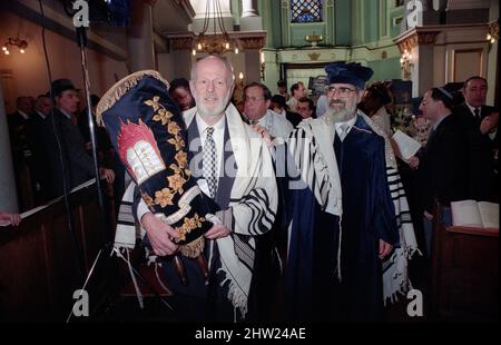 Die neue Sefer Tora wird um die Synagoge getragen, damit die Gemeinde ihre Achtung zollt. Der Oberrabbiner Jonathan Sacks war Ehrengast für die Aufnahme der letzten Briefe in eine neue Sefer-Torah in der Synagoge der hebräischen Kongregation Singers Hill am Sonntag, dem 15. März 1998. Mitglieder der Gemeinde sowie der Oberrabbiner fügten jeweils einen einzigen Brief hinzu. Stockfoto