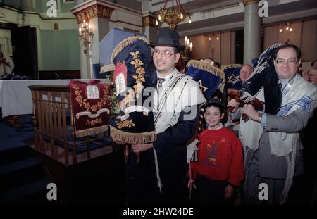 Die neue Sefer Tora wird um die Synagoge getragen, damit die Gemeinde ihre Achtung zollt. Der Oberrabbiner Jonathan Sacks war Ehrengast für die Aufnahme der letzten Briefe in eine neue Sefer-Torah in der Synagoge der hebräischen Kongregation Singers Hill am Sonntag, dem 15. März 1998. Mitglieder der Gemeinde sowie der Oberrabbiner fügten jeweils einen einzigen Brief hinzu. Stockfoto