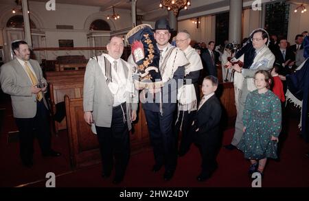 Die neue Sefer Tora wird um die Synagoge getragen, damit die Gemeinde ihre Achtung zollt. Der Oberrabbiner Jonathan Sacks war Ehrengast für die Aufnahme der letzten Briefe in eine neue Sefer-Torah in der Synagoge der hebräischen Kongregation Singers Hill am Sonntag, dem 15. März 1998. Mitglieder der Gemeinde sowie der Oberrabbiner fügten jeweils einen einzigen Brief hinzu. Stockfoto