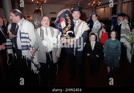 Die neue Sefer Tora wird um die Synagoge getragen, damit die Gemeinde ihre Achtung zollt. Der Oberrabbiner Jonathan Sacks war Ehrengast für die Aufnahme der letzten Briefe in eine neue Sefer-Torah in der Synagoge der hebräischen Kongregation Singers Hill am Sonntag, dem 15. März 1998. Mitglieder der Gemeinde sowie der Oberrabbiner fügten jeweils einen einzigen Brief hinzu. Stockfoto