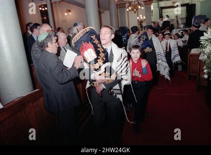 Die neue Sefer Tora wird um die Synagoge getragen, damit die Gemeinde ihre Achtung zollt. Der Oberrabbiner Jonathan Sacks war Ehrengast für die Aufnahme der letzten Briefe in eine neue Sefer-Torah in der Synagoge der hebräischen Kongregation Singers Hill am Sonntag, dem 15. März 1998. Mitglieder der Gemeinde sowie der Oberrabbiner fügten jeweils einen einzigen Brief hinzu. Stockfoto