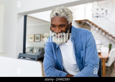 Lächelnder bärtiger afroamerikanischer Mann, der im Wohnzimmer auf den Laptop schaute Stockfoto