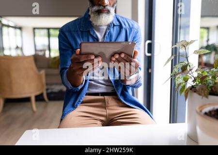 Mittelteil eines hochrangigen afroamerikanischen Mannes, der zu Hause ein digitales Tablet verwendet Stockfoto