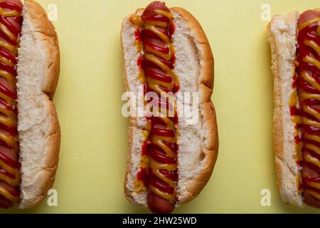 Direkt über Nahaufnahme von Saucen auf Hot Dogs nebeneinander auf gelbem Hintergrund angeordnet Stockfoto