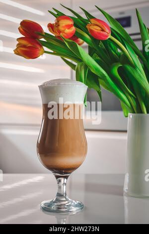 Kaffee in der Küche. Latte Macchiato mit Blumen im Hintergrund. Stockfoto