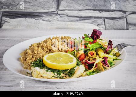 Frisches, leckeres vegetarisches Mittagessen. Fisch mit Salat und Quinoa auf weißen Tellern in der Küche. Stockfoto