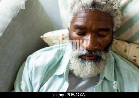 Blick aus der Ferne auf den pensionierten afroamerikanischen Senioren mit weißem Bart, der zu Hause auf dem Sofa schläft Stockfoto