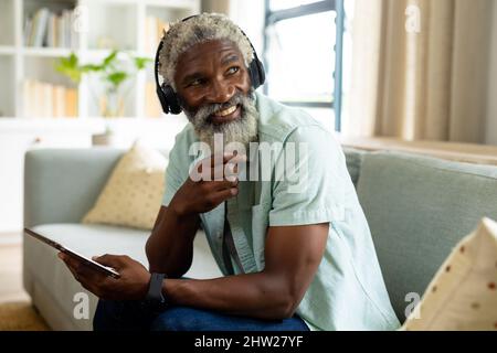 Lächelnder afroamerikanischer Mann, der über Kopfhörer Musik hört, während er mit einem digitalen Tablet sitzt Stockfoto