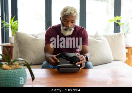 Bärtiger afroamerikanischer Senior mit Virtual-Reality-Headset auf dem Sofa im Wohnzimmer Stockfoto