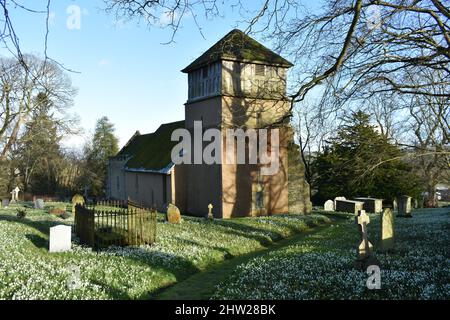 Nahaufnahme der Kirche Shipton, Shropshire, mit Schneeglöckchen im Grabehof an einem sonnigen Februartag Stockfoto