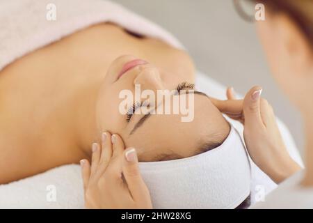 Entspannte Frau lindert Stress, während sie eine professionelle Gesichts- und Kopfmassage im Spa-Salon erhält. Stockfoto