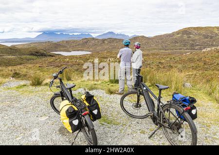 Zwei Radler auf Elektrofahrrädern blicken nach Norden über Loch Dhughaill auf der Sleat Peninsula im Süden der Isle of Skye, Highland, Schottland, Großbritannien Stockfoto