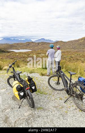 Zwei Radler auf Elektrofahrrädern blicken nach Norden über Loch Dhughaill auf der Sleat Peninsula im Süden der Isle of Skye, Highland, Schottland, Großbritannien Stockfoto