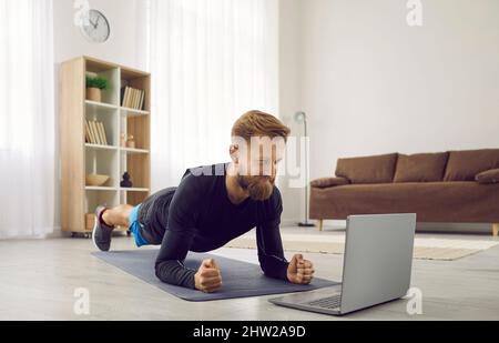 Ein Mann, der während seines Heimtrainings mit einem Online-Fitnesstrainer eine Plank-Übung macht Stockfoto