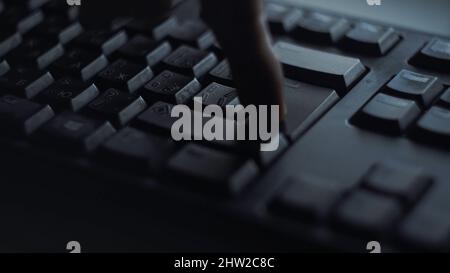 Nahaufnahme Mann drückt Tastatur-Taste. Mann drückt Taste geben Computertastatur. Die Hand des Mannes drückt die Tastatur im Licht des Computerbildschirms. Stockfoto