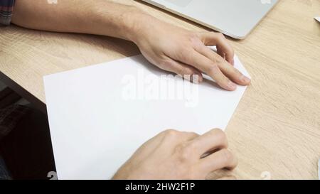 Hände machen Origami-Figur. Nahaufnahme der männlichen Hände mit einem weißen Blatt Papier für die Herstellung von Origami auf Holztisch Hintergrund, Konzept der Kreativität. Stockfoto