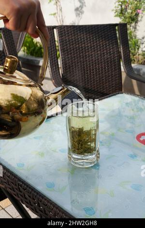 Frisch zubereiteter Aufguss von Chinatee mit kochendem Wasser, das aus einer Teekane mit heißem Wasser in dicke, geschnittene chinesische Teeblätter in Glasgläsern gegossen wird. Stadt Songpan im Norden von Sichuan, China. (125) Stockfoto