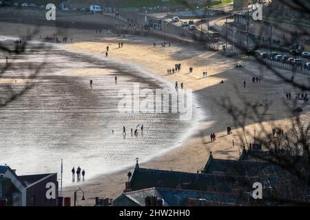 Menschen, die am Strand in der Sonne spazieren, in Scarborough, North Yorkshire, England Stockfoto