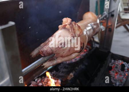 Schwein wird langsam vom Grill auf Spit in traditioneller Art, mit Holzkohle, fettes gebratenes Fleisch gekocht Stockfoto