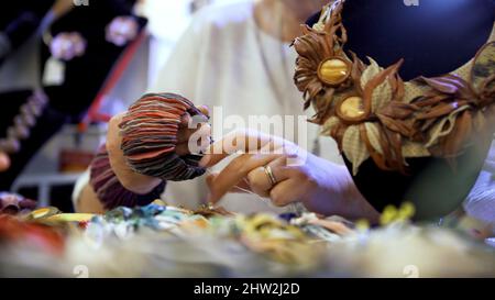 Frau mit einem handgefertigten Armband aus dicken Stoffstücken, die wie Blütenblätter aussehen. Art. Interieur einer Werkstatt mit handwerklichem Schmuck Stockfoto