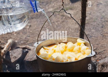 Wasser aus einer großen Plastikflasche in einen Kessel mit Kartoffel, Campingmahlzeit Stockfoto