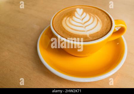 Gelbe Tasse Cappuccino mit Latte-Kunst steht auf einem Holztisch Stockfoto