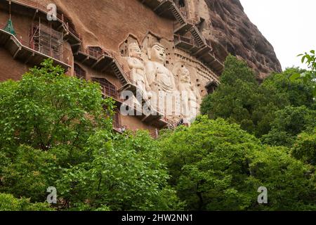 Stufen und Gehwege, die an der schieren Felswand befestigt sind, ermöglichen es den Besuchern, die alten geschnitzten Statuen des buddhistischen Tages zu sehen, an dem sie befestigt und in die Steinoberfläche der Felswand gehauen ist. Die Maijishan-Grotten, früher als Maichishan romanisiert, Sind eine Reihe von 194 Höhlen, die an der Seite des Hügels von Majishan in Tianshui, Provinz Gansu, China, geschnitten wurden. (67/125) Stockfoto