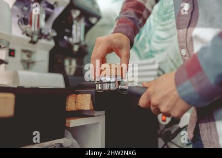 Nahaufnahme des Baristas, der gemahlenen Kaffee zum Espressokochen eintampft Stockfoto