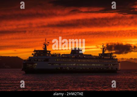 Seattle, USA. 2. März 2022. Sonnenuntergang während eines Sturms am Wasser, während eine Fähre vorbeifährt. Stockfoto