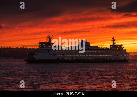 Seattle, USA. 2. März 2022. Sonnenuntergang während eines Sturms am Wasser, während eine Fähre vorbeifährt. Stockfoto