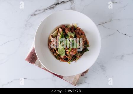 Frischer Schweinskochsalat mit Huhn und Gemüse in einem Gericht isoliert auf matter Draufsicht auf grauem Marmorboden Stockfoto