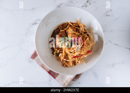Nördliche thailändische khao Soi Chicken-Kurvennudeln in einem Gericht isoliert auf matter Draufsicht auf grauem Marmorboden Stockfoto